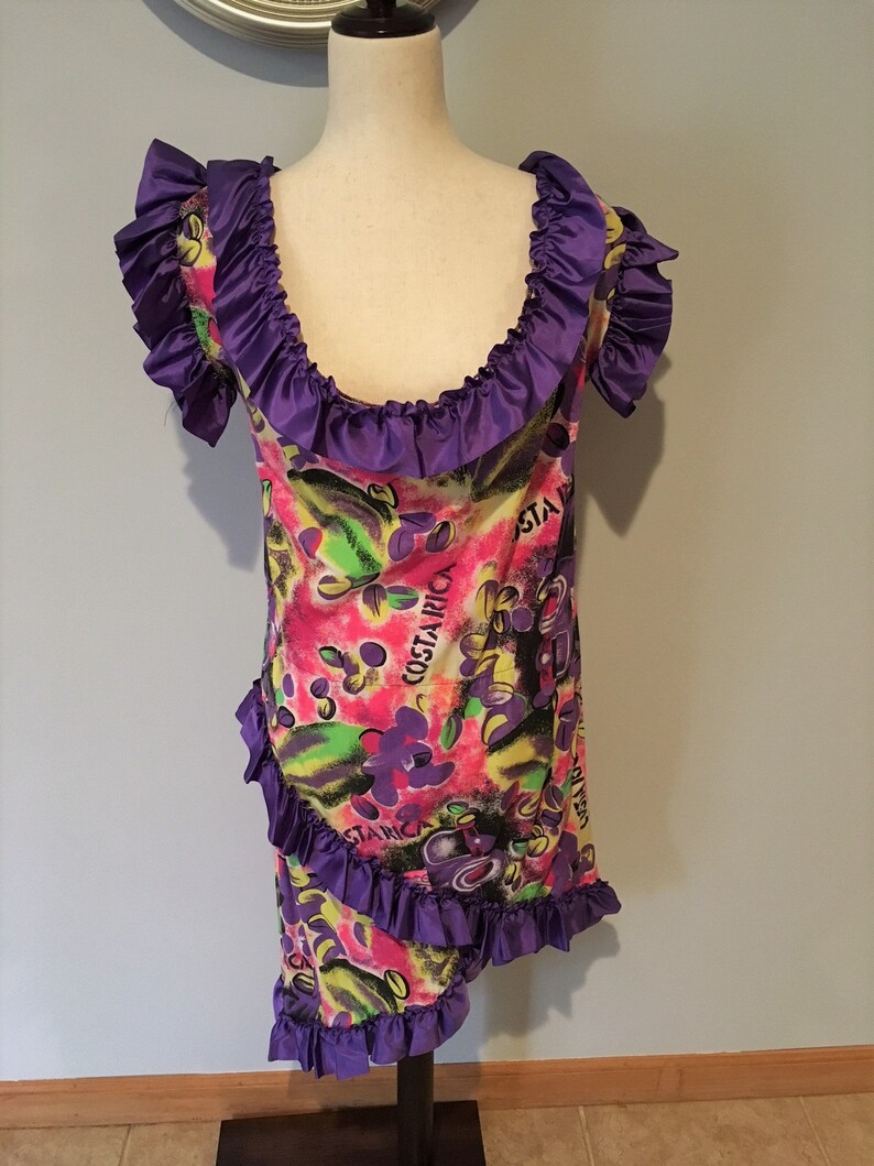 Pode incluir: Um vestido roxo e branco com estampa floral e o texto "Costa Rica" na frente. O vestido tem um decote e uma bainha com babados.