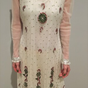May include: White long-sleeved dress with intricate embroidery and sequins. The dress features a round neckline and a flowing skirt.