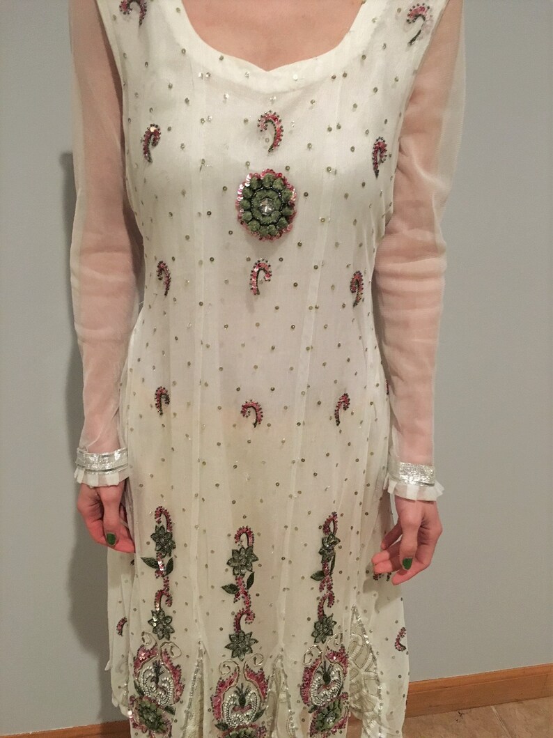 May include: White long-sleeved dress with intricate embroidery and sequins. The dress features a round neckline and a flowing skirt.