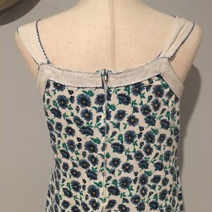 May include: A white dress with a blue floral pattern and a zipper down the back. The dress has thin straps and a white trim around the neckline.