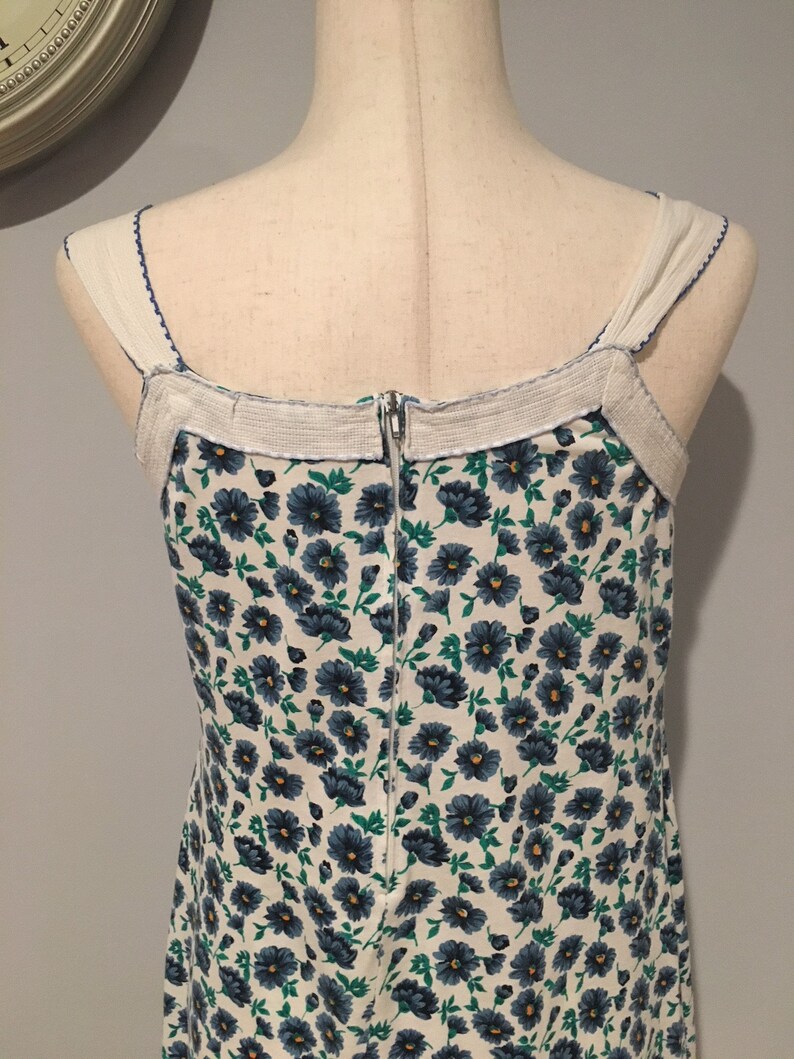 May include: A white dress with a blue floral pattern and a zipper down the back. The dress has thin straps and a white trim around the neckline.
