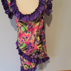 Pode incluir: Um vestido roxo e branco com decote e bainha com babados. O vestido tem uma estampa colorida com as palavras "Costa Rica" e um design floral.