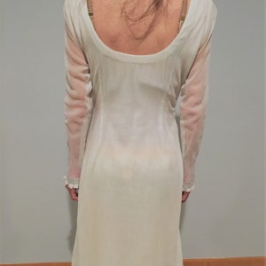 May include: A white sheer tunic with a scoop neck and long sleeves. The tunic has a lace trim around the neckline and hem.