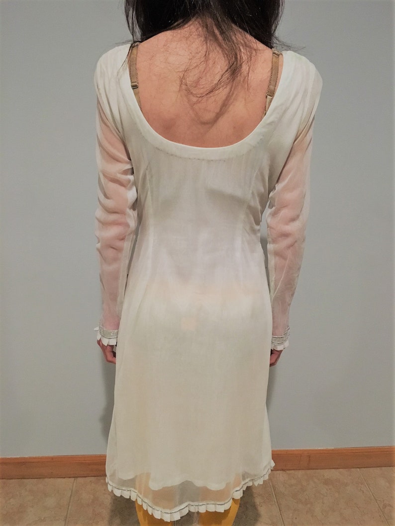 May include: A white sheer tunic with a scoop neck and long sleeves. The tunic has a lace trim around the neckline and hem.