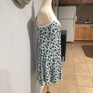 May include: A white dress with a blue and green floral pattern. The dress has thin straps and a fitted bodice. The dress is on a white mannequin.