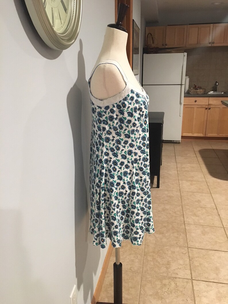 May include: A white dress with a blue and green floral pattern. The dress has thin straps and a fitted bodice. The dress is on a white mannequin.