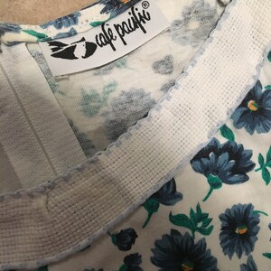 May include: A white fabric with a blue floral pattern and a white label with the text "cafe  paiffi" in black lettering.