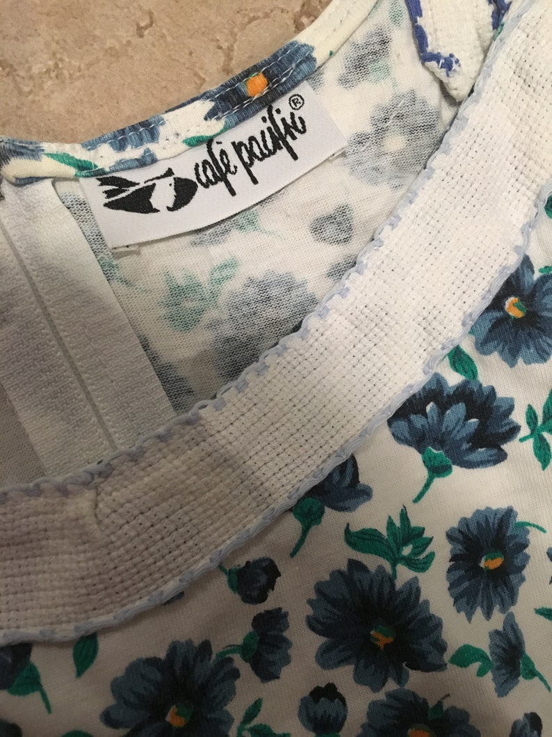 May include: A white fabric with a blue floral pattern and a white label with the text "cafe  paiffi" in black lettering.