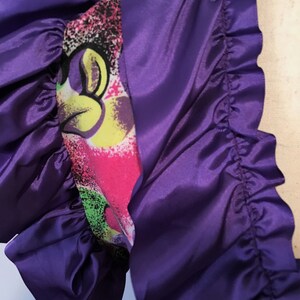Pode incluir: Tecido de cetim roxo com uma borda franjada. O tecido tem uma estampa colorida com um personagem de desenho animado.