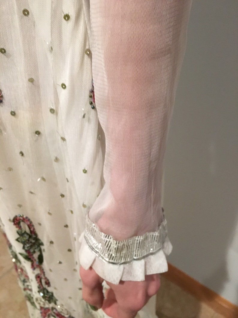 May include: White sheer long-sleeved dress with a beaded trim and a floral pattern. The dress has a ruffled cuff.
