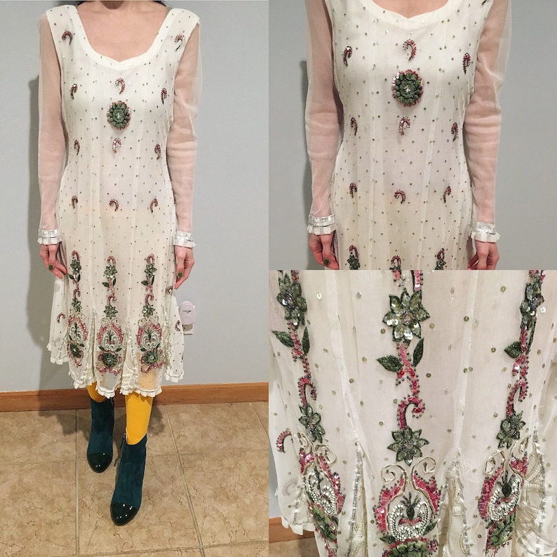 May include: A white sheer dress with pink and green floral embroidery. The dress has a long sleeve and a round neckline. The dress is decorated with sequins and beads.