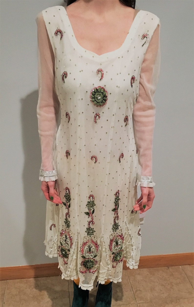 May include: A white sheer dress with long sleeves and a round neckline. The dress is decorated with pink and green floral embroidery and sequins.