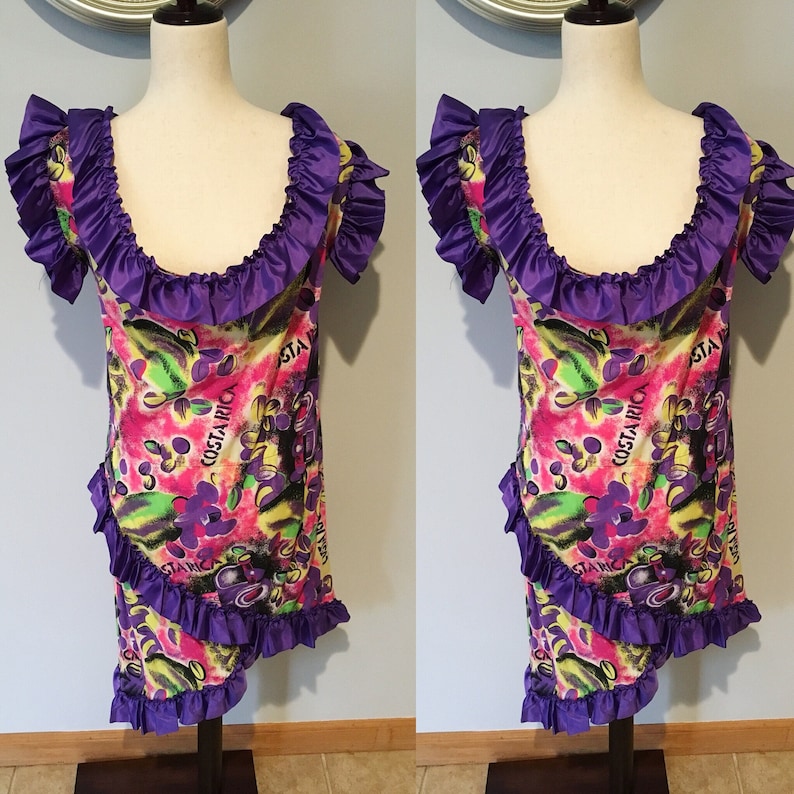 Pode incluir: Um vestido roxo e amarelo com estampa floral e babados. O vestido tem o texto "COSTARICA" impresso.