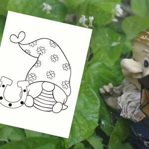 May include: Black and white coloring page featuring a gnome wearing a hat with shamrocks and holding a horseshoe.