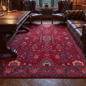 May include: A library room featuring a large red area rug with blue and cream patterns, a wooden desk, two leather armchairs, and a tufted leather sofa. The space includes floor-to-ceiling bookshelves, a chandelier, and a tall window with curtains.