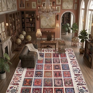 May include: A large, rectangular area rug with a cream-colored background and a repeating pattern of colorful, square motifs. The squares feature intricate designs in red, blue, orange, and other hues. The rug is in a room with a leather sofa, bookshelves, and a chandelier.