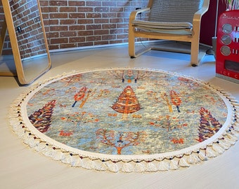 Puede incluir: Una alfombra redonda de color azul y crema con un borde de flecos. La alfombra presenta un patrón repetitivo de árboles estilizados en tonos naranja, rojo y morado.