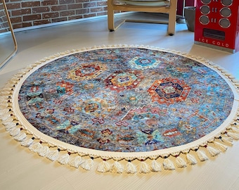 May include: A round, multi-colored rug with a fringe border. The rug has a blue, red, orange, and yellow pattern. The rug is on a light wood floor.