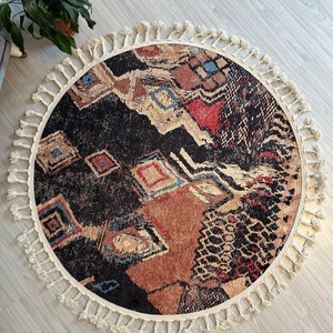 May include: A round rug with a black, brown, red, and blue geometric pattern. The rug has a white fringe border.