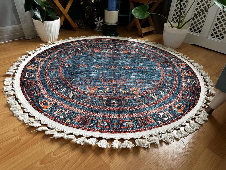 May include: A round blue and red rug with a white fringe. The rug has a traditional pattern with intricate details.