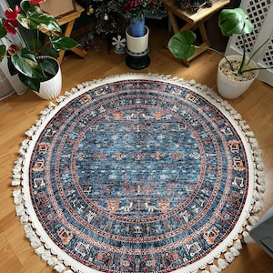 May include: A round blue rug with a white fringe border. The rug has a geometric pattern in shades of red, orange, and blue. The rug is on a wooden floor.