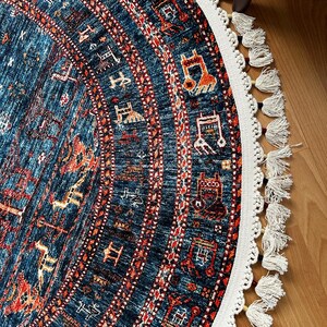 May include: A round rug with a blue background and intricate red, orange, and white patterns. The rug has a white fringe border with tassels.