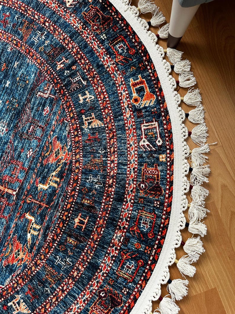 May include: A round rug with a blue background and intricate red, orange, and white patterns. The rug has a white fringe border with tassels.