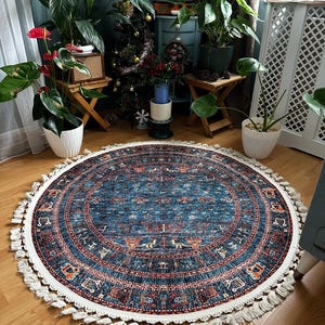 May include: A round blue and white rug with a fringe border. The rug has a traditional pattern with geometric shapes and floral motifs. The rug is on a wooden floor.