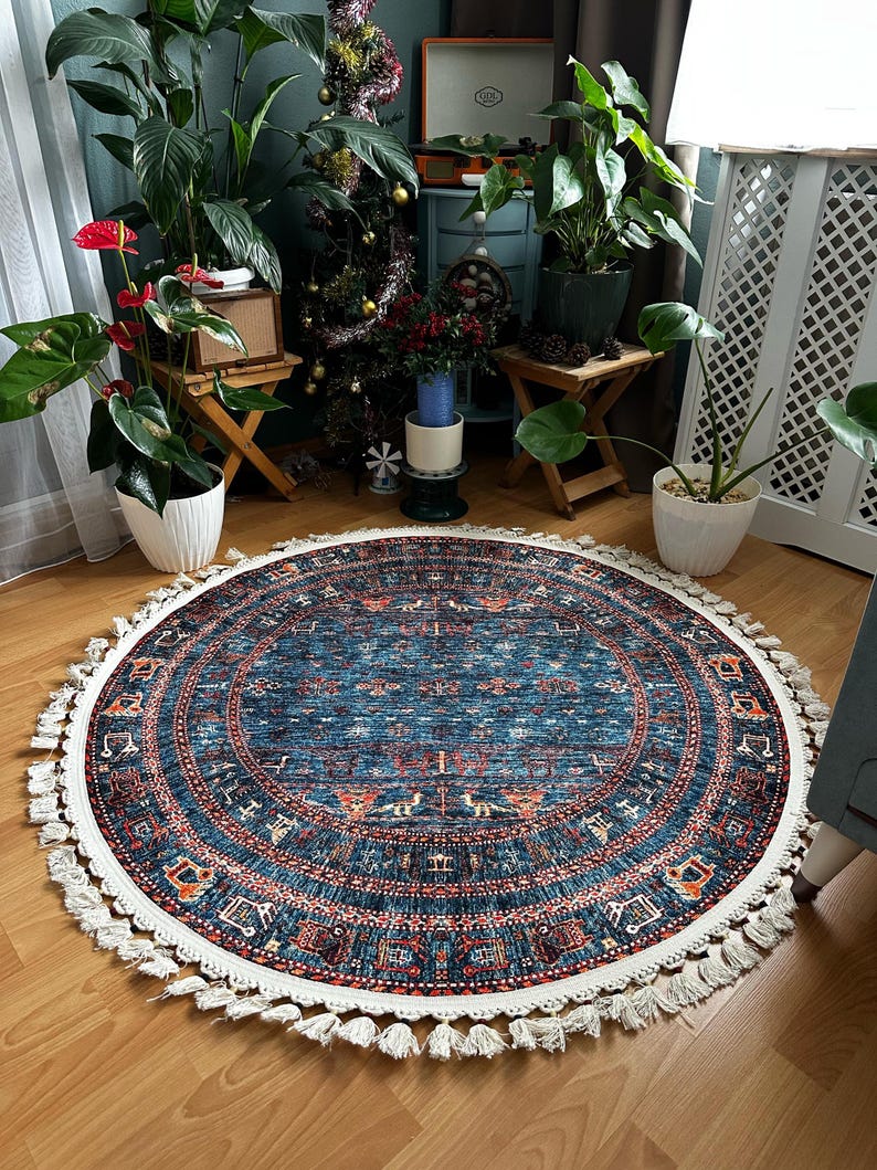 May include: A round blue and white rug with a fringe border. The rug has a traditional pattern with geometric shapes and floral motifs. The rug is on a wooden floor.