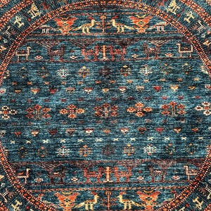 May include: A round rug with a blue background and intricate patterns in shades of orange, red, and white. The rug features a central medallion with a repeating design of stylized birds and geometric shapes.