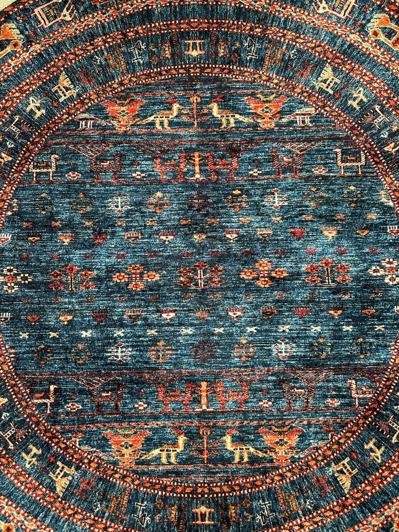 May include: A round rug with a blue background and intricate patterns in shades of orange, red, and white. The rug features a central medallion with a repeating design of stylized birds and geometric shapes.