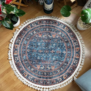 May include: A round blue rug with a white fringe border. The rug has a geometric pattern in shades of red, orange, and white.