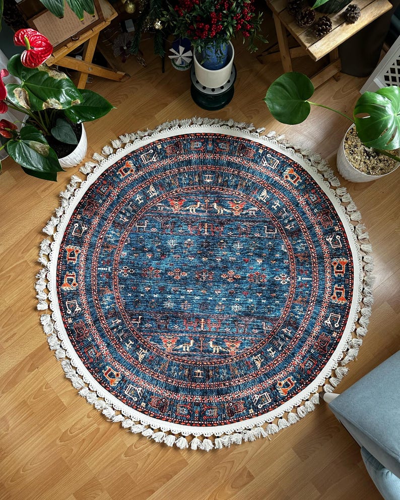 May include: A round blue rug with a white fringe border. The rug has a geometric pattern in shades of red, orange, and white.