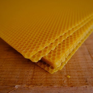 Puede incluir: Un montón de láminas de base de cera de abeja amarilla para apicultura. Las láminas están hechas de un patrón de panal y están listas para colocarse en una colmena.