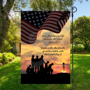 May include: A garden flag with a silhouette of soldiers standing at sunset. The flag is waving in the wind and has the American flag design. The text on the flag reads: "Our flag does not fly because the wind moves it. It flies with the breath of each soldier who died protecting it."