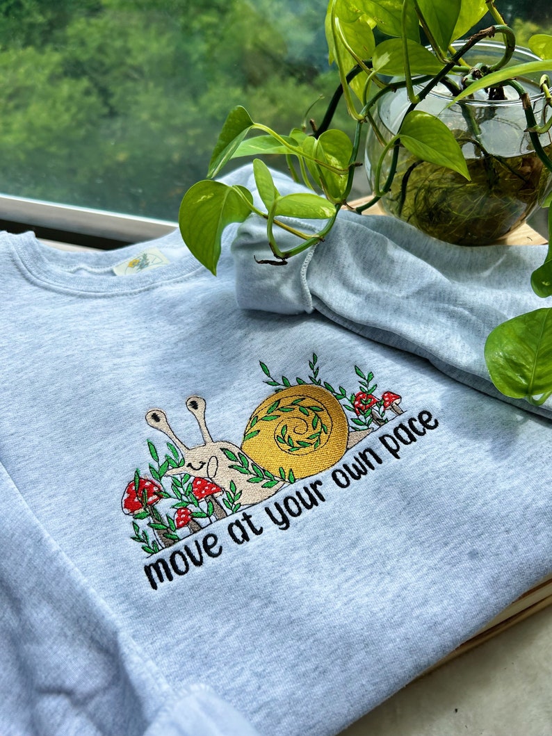 May include: A light blue sweatshirt with an embroidered snail design and the text "move at your own pace".