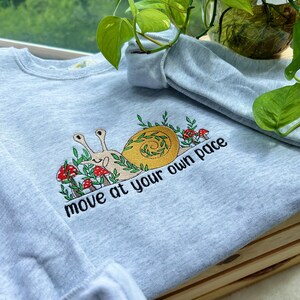May include: Light blue sweatshirt with an embroidered snail design and the text "move at your own pace".