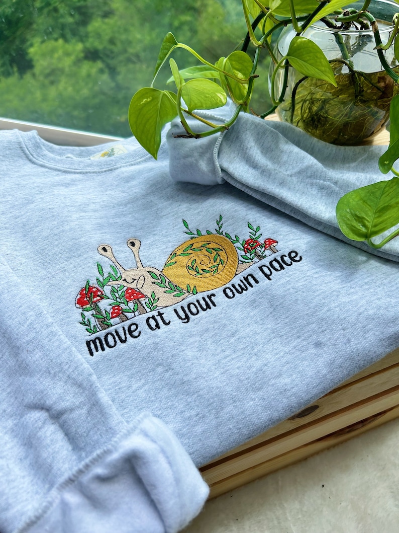 May include: Light blue sweatshirt with an embroidered snail design and the text "move at your own pace".
