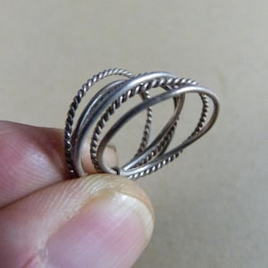 May include: A set of three interlocking silver-toned rings. Two of the rings feature a twisted rope-like texture, while the third ring has a smooth, plain surface. The rings are connected together to form a single cohesive unit of jewellery.