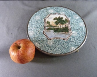 Sottopentola antico in ceramica decorato con una riva di fiume e una pigna.