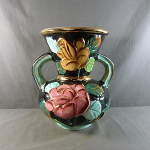 May include: A vintage ceramic vase with a black base, adorned with embossed pink and yellow floral designs. The vase features two handles and a gold rim, adding a touch of elegance to its design. The vase is a decorative item.