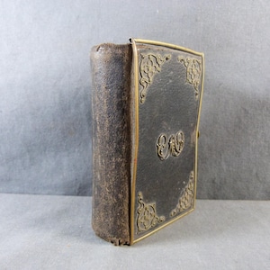 May include: A vintage leather-bound book with gold-colored decorative accents and a monogram on the front cover.
