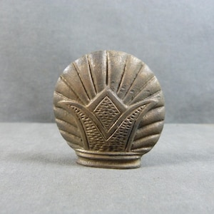 Peut inclure: Un bouton de meuble décoratif de couleur bronze, avec un motif en forme d'éventail. Le bouton présente un motif détaillé de lignes rayonnantes et un motif floral ou coquillage stylisé à la base. Le bouton est probablement en métal.