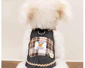 May include: A dog harness with a gray denim base and a brown plaid pocket. The pocket has a label with a cartoon bear and the word "Hello". The harness has a decorative trim and wooden buttons.
