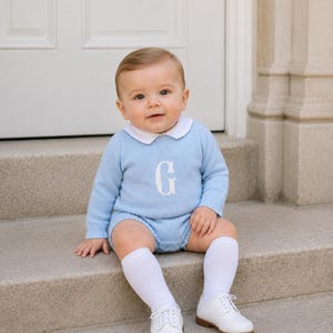 Può includere: Un maglione in maglia a maniche lunghe color azzurro con colletto bianco e una lettera G ricamata in bianco sul petto, abbinato a pantaloncini in maglia azzurri, calzettoni bianchi al ginocchio e scarpe eleganti bianche con lacci.