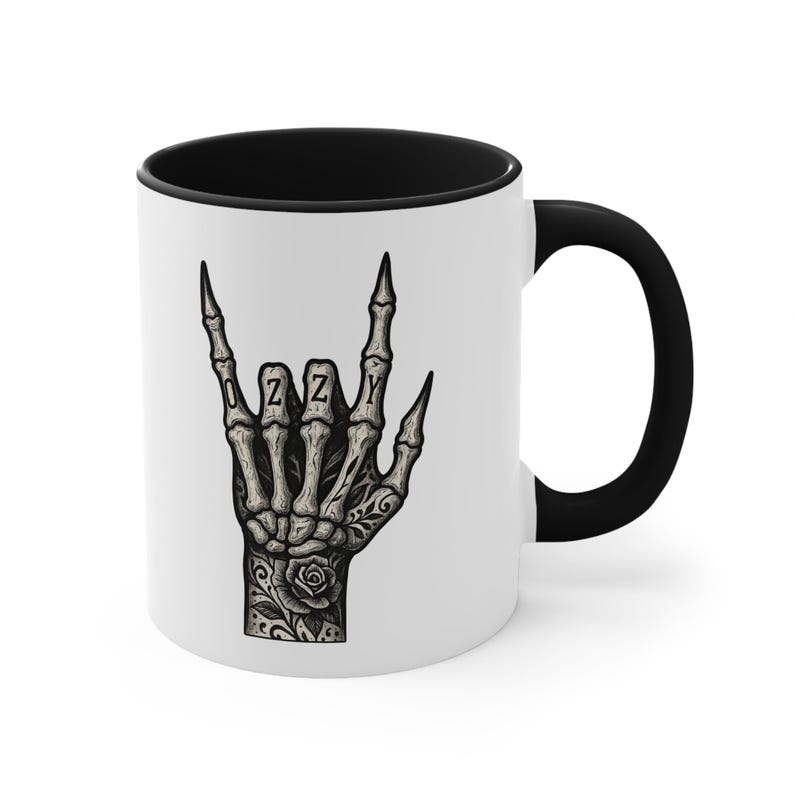 Puede incluir: Taza de cer&aacute;mica blanca con interior y asa negros. La taza presenta una mano esquel&eacute;tica en el gesto de rock and roll, con el nombre "OZZY" escrito en los nudillos. Un tatuaje de rosa es visible en la mano.