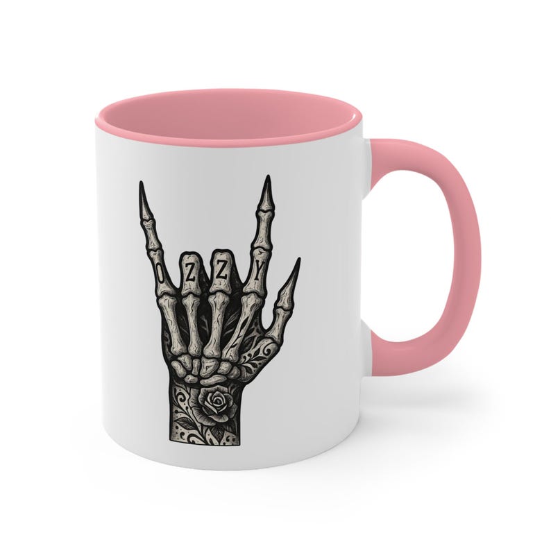 Puede incluir: Taza de cer&aacute;mica blanca con interior y asa rosas. La taza presenta una ilustraci&oacute;n en blanco y negro de una mano esquel&eacute;tica haciendo el gesto de rock and roll, con el nombre "OZZY" escrito en los nudillos.