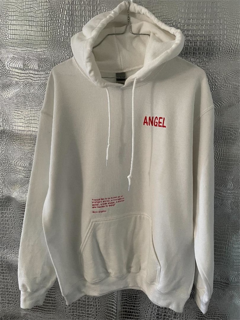May include: White hooded sweatshirt with a red embroidered "ANGEL" on the front and a red embroidered quote on the pocket. The quote reads: "I would like to be known as an intelligent woman, a courageous woman, a woman who dares to be a woman who teaches by being."