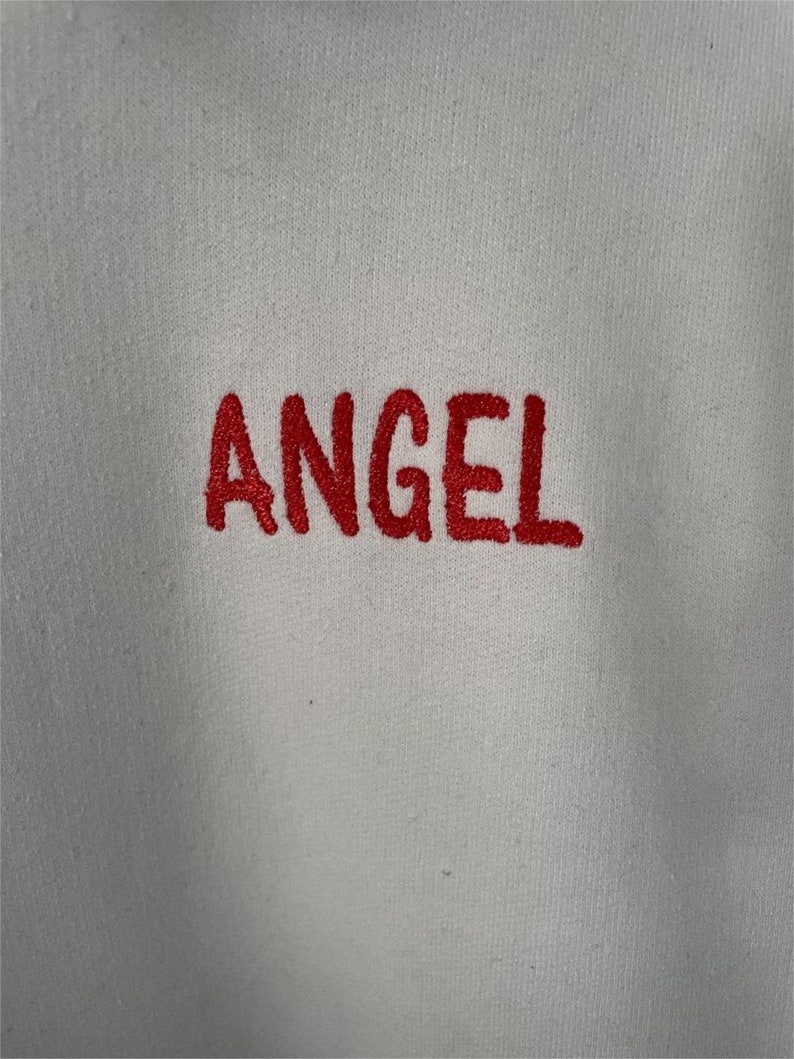 May include: White sweatshirt with the word "ANGEL" embroidered in red.