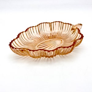 Puede incluir: Un plato de servir de vidrio vintage con un borde festoneado y un diseño acanalado. El plato está hecho de vidrio transparente con un ligero tono ámbar.